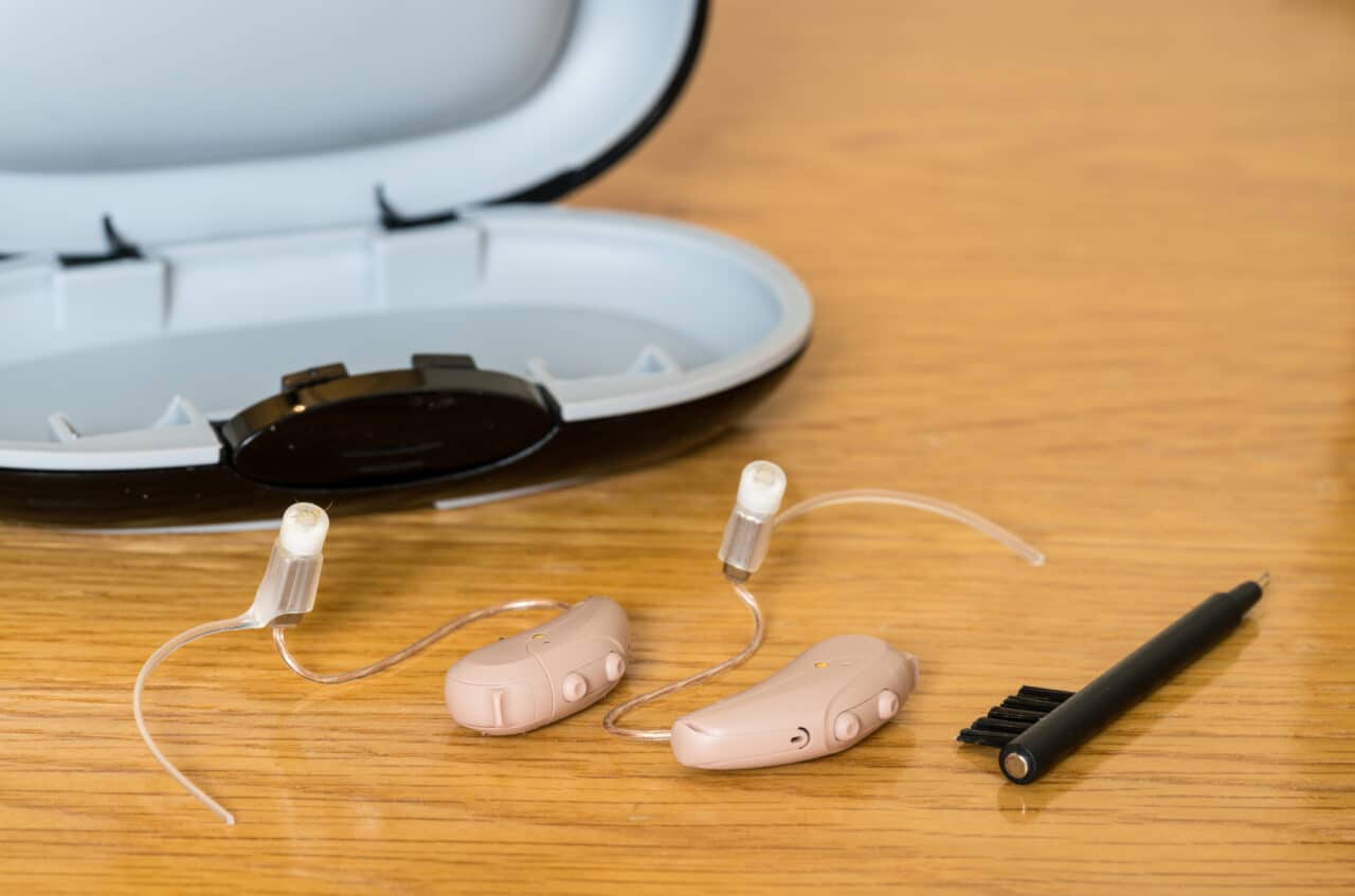 Close up of hearing aids with their case and a cleaning brush.