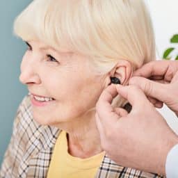 Audiologist fitting a cheerful senior woman with a hearing aid.